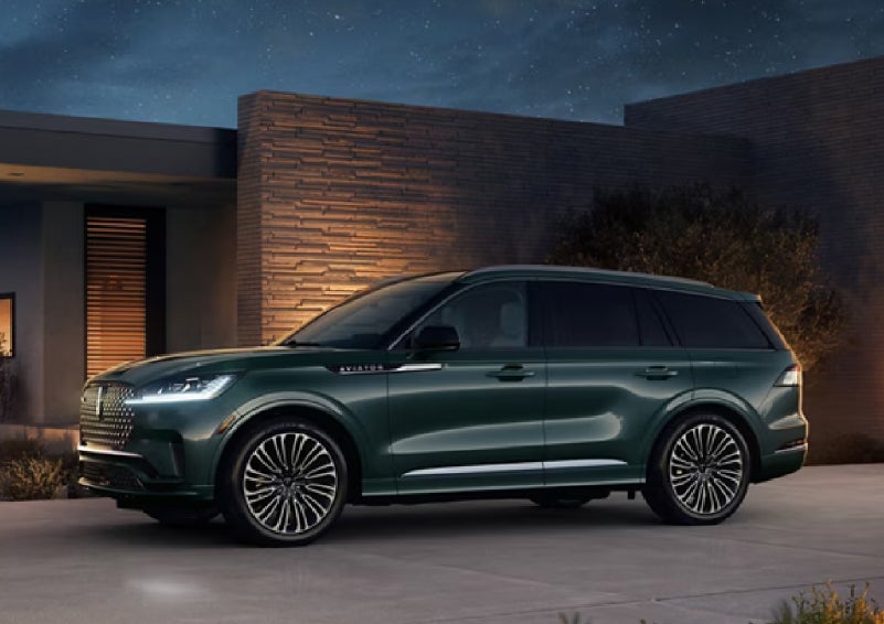 A green 2027 Lincoln Aviator® SUV is parked outside a contemporary home. | Lincoln of New Bern in New Bern NC