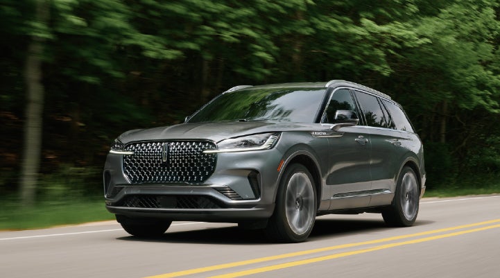 A 2027 Lincoln Aviator® SUV is being driven down a road lined with trees. | Lincoln of New Bern in New Bern NC